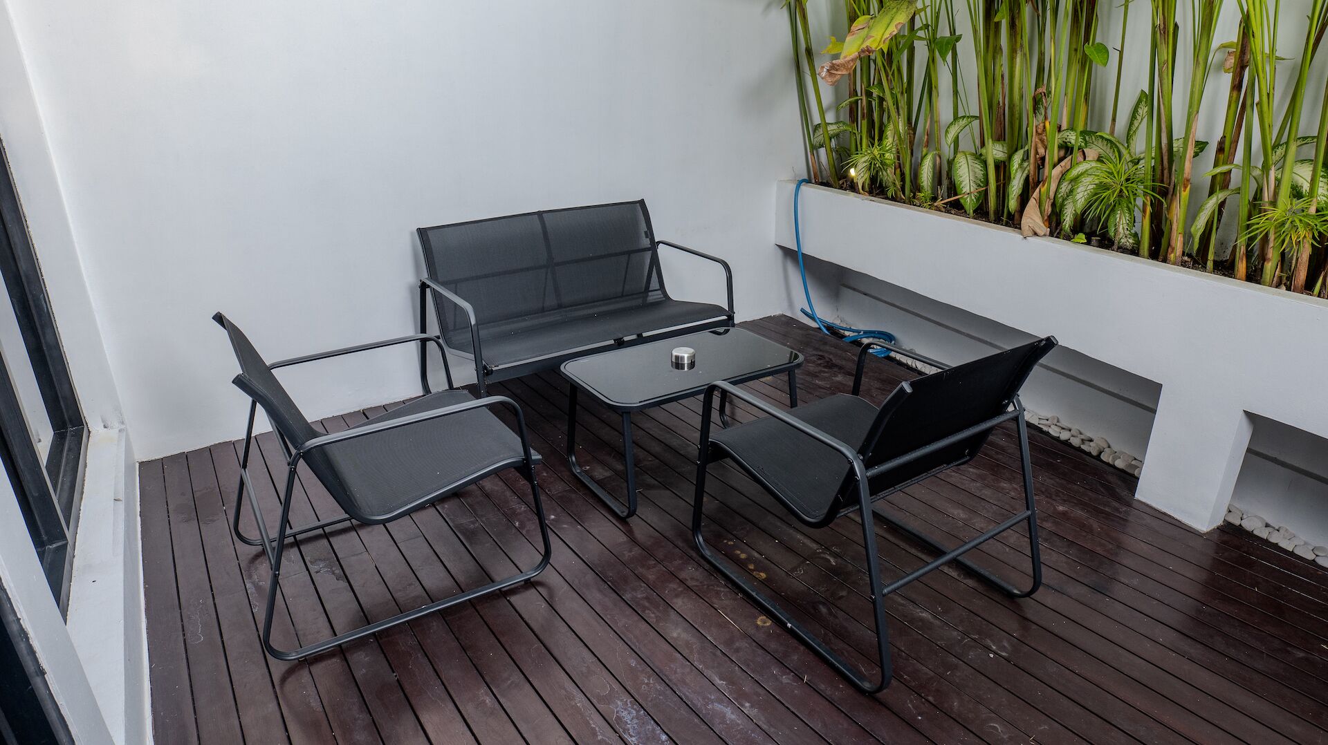 A small outdoor patio with a wooden deck, a metal table, and four black chairs.