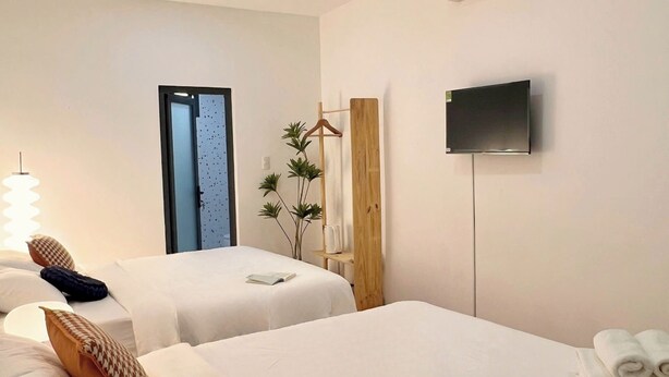 A hotel room with two beds, a TV, an air conditioning unit, and a door leading to another room. - Ky Dong Hotel by N Retreat (Ho Chi Minh City)