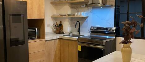 Una cucina moderna con mobili in legno, elettrodomestici in acciaio inossidabile, un piano di lavoro in marmo e illuminazione a sospensione.