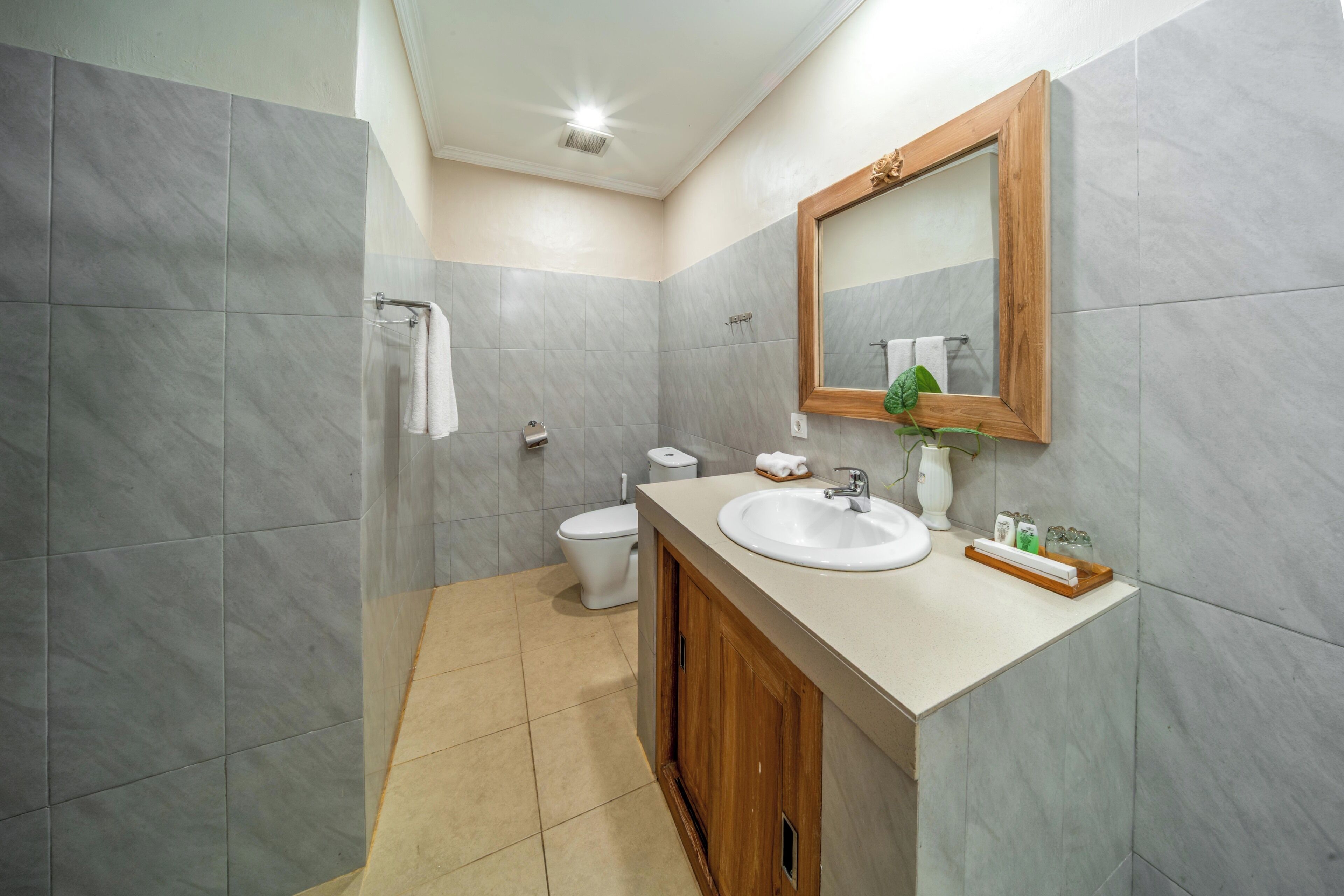 A bathroom with grey tiles, a white sink, a wooden cabinet, a mirror, and a toilet.