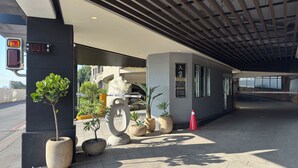 Una entrada moderna a un edificio con una escultura de piedra, plantas en macetas y un camino despejado hacia la entrada.