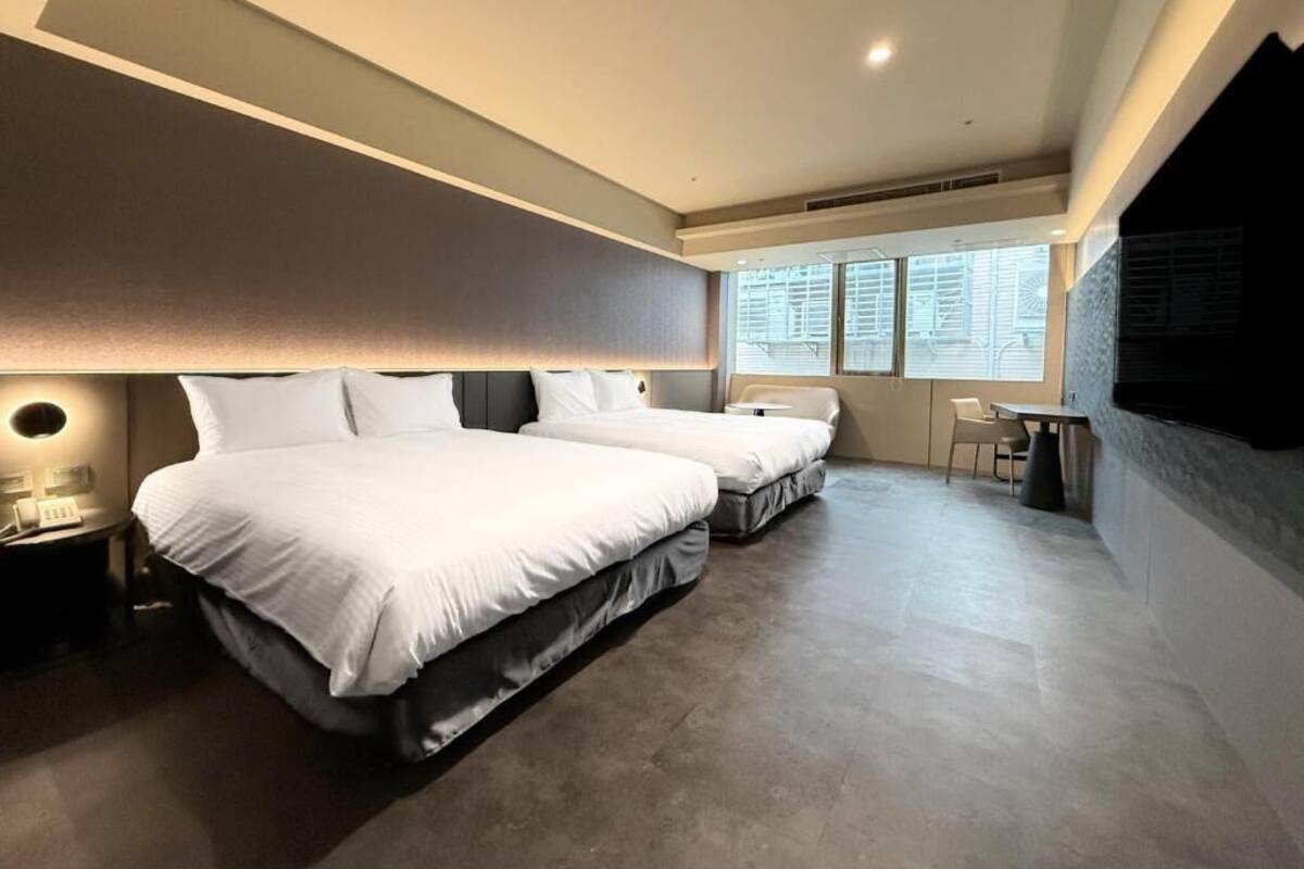 A modern hotel room with two beds, a desk, and a chair.