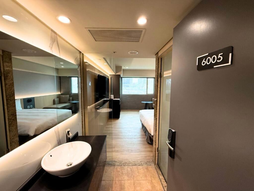 Una habitación de hotel moderna con un espejo grande, un lavamanos, una cama y una mesita pequeña.
