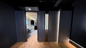 Un moderno vestíbulo de hotel con piso de madera, paredes oscuras y una puerta de vidrio que da a un área de descanso.