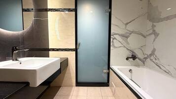 A modern bathroom with a large mirror, a white sink, a bathtub, and a frosted glass door.