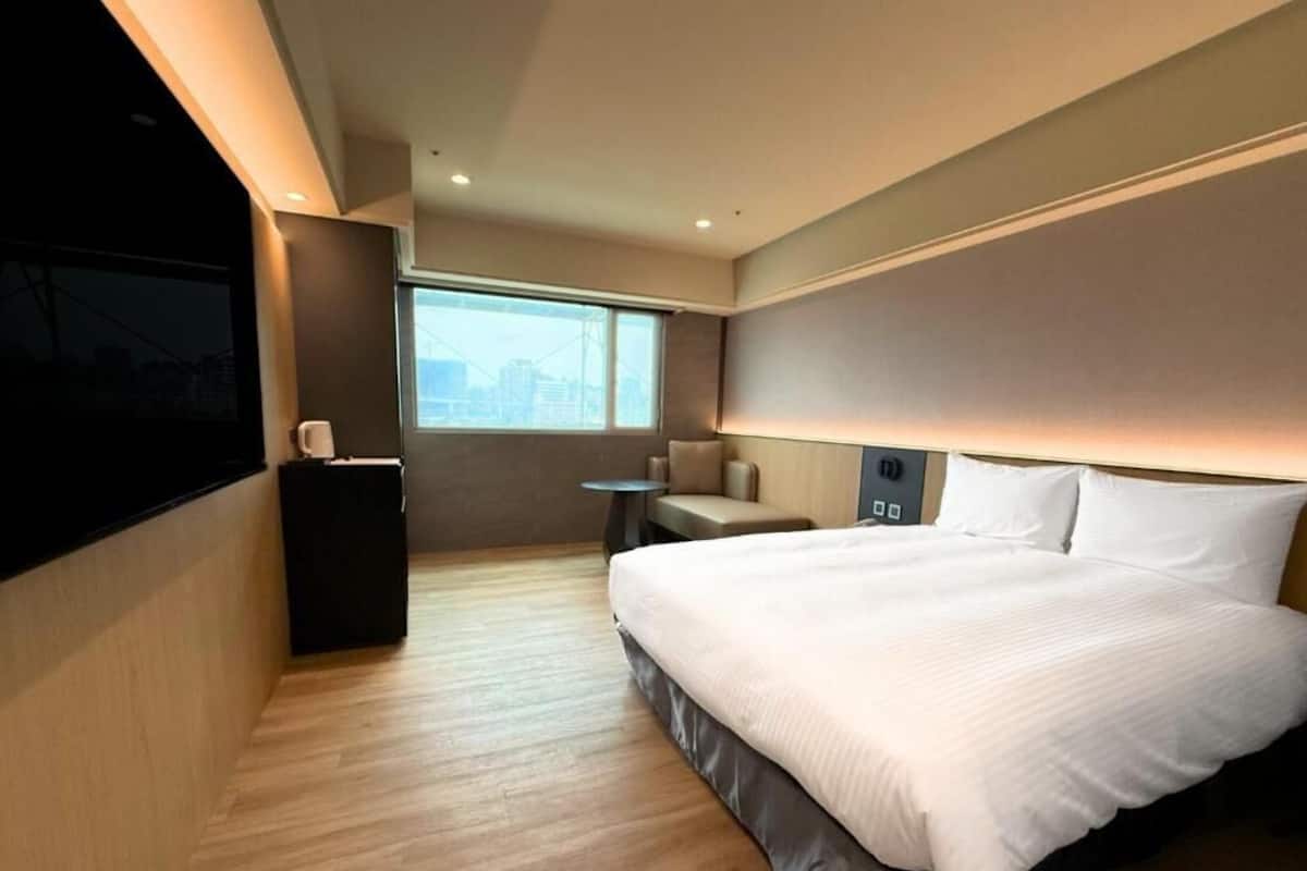 A modern hotel room with a large bed, a desk, a chair, and a TV mounted on the wall.