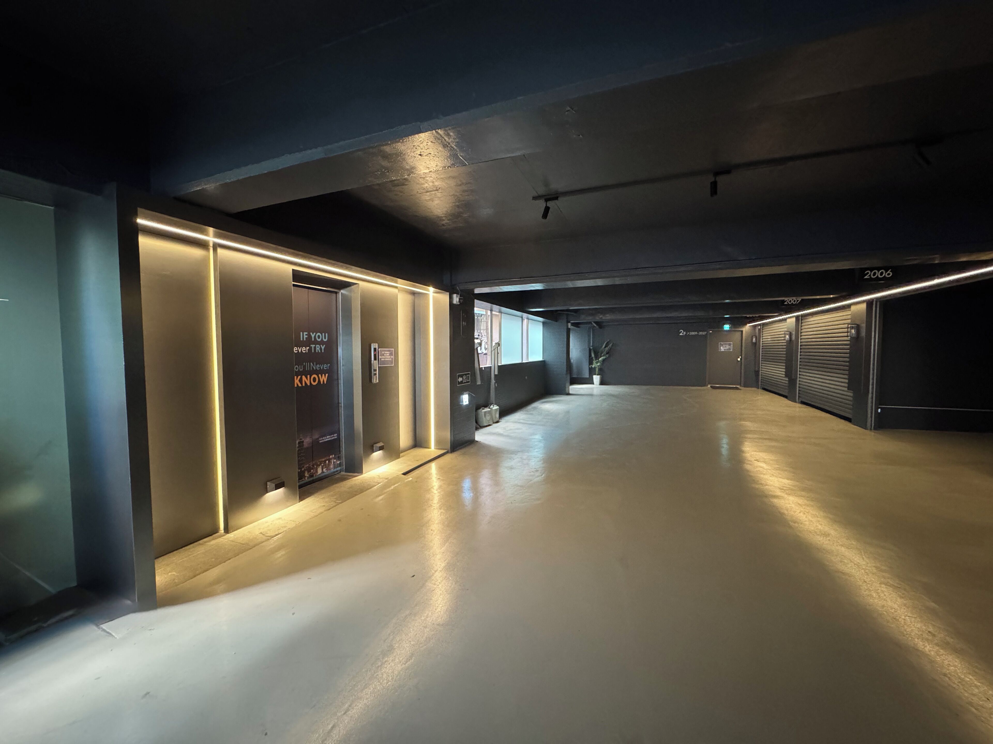 A clean, modern hallway with a polished concrete floor, recessed lighting, and closed garage doors numbered 2006 and 2007.