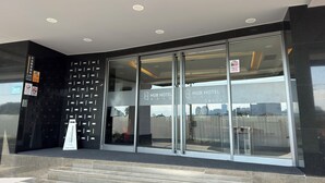 La entrada de un hotel moderno con puertas de vidrio, un mostrador de recepción y una escalera que sube.
