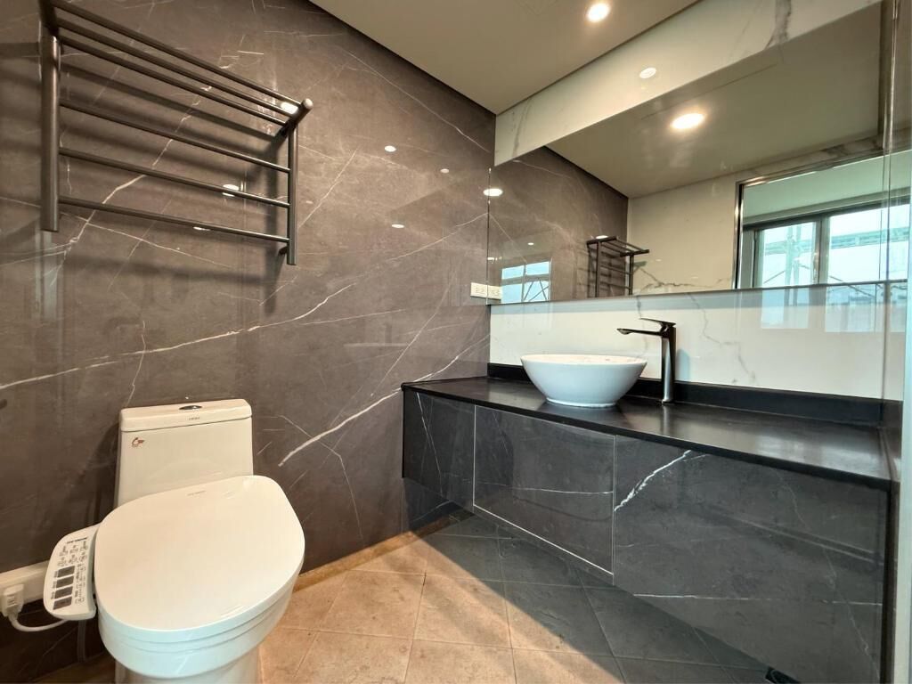 A modern bathroom with a toilet, a sink with a large basin, a towel rack, and a mirror.
