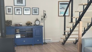 Una sala de estar con un mueble de entretenimiento azul, una escalera de madera y vista a un edificio a través de una ventana.