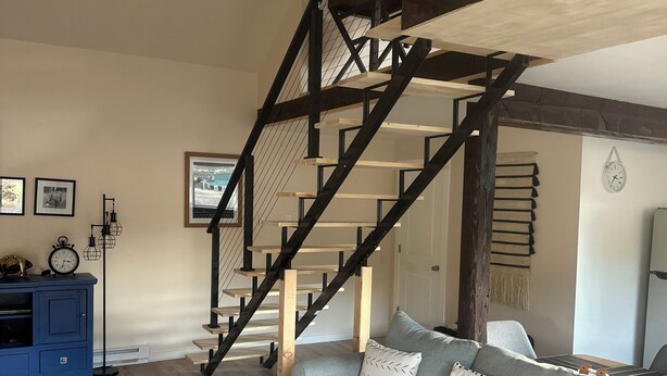Una sala de estar con una escalera, un aparador azul, un sofá gris y una mesa de centro de madera.