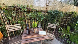 A wooden table with a bottle of wine, a glass, and a newspaper. Two wooden chairs are placed around the table. - Ideal for Solos HTub Retro Decor Parking WiFi (Newton Abbot)
