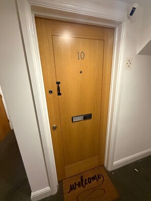 A wooden door with a number plate, a doorbell, and a welcome mat. - Guildford Court Apartment Colchester (Colchester)