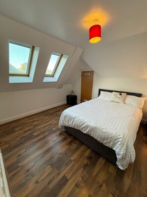 A bedroom with a large bed, skylights, and a red pendant light. - Guildford Court Apartment Colchester (Colchester)