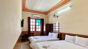 Quarto de hotel com duas camas, ar condicionado, uma escrivaninha, uma cadeira e uma janela com cortinas.