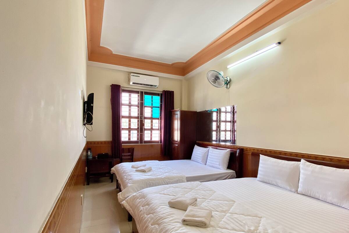 A hotel room with two beds, an air conditioning unit, a desk, a chair, and a window with curtains.