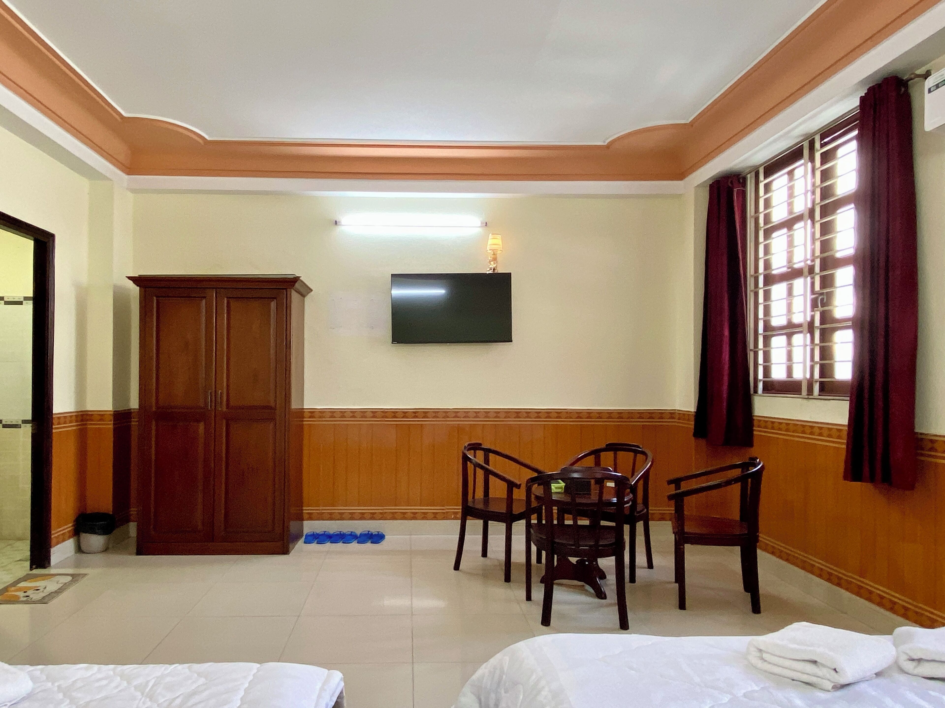 Habitación de hotel con cama, escritorio con silla, televisor montado en la pared y ventana con cortinas.