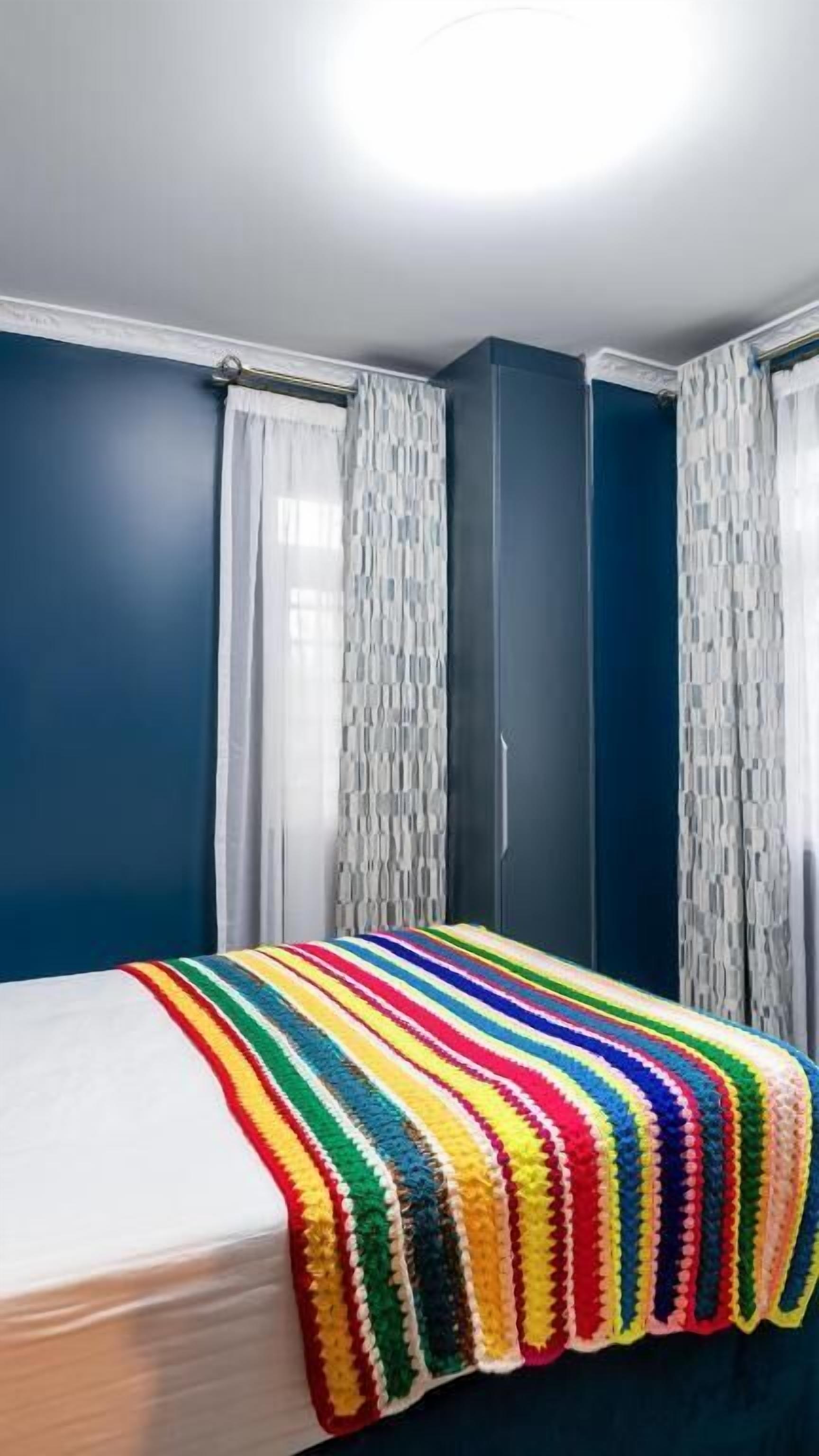 Ein Schlafzimmer mit Bett, blauen Wänden und weißen Vorhängen.