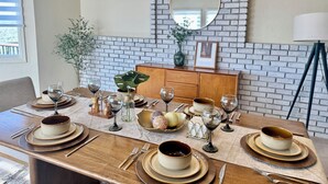 Une table à manger dressée avec de nombreuses assiettes, des bols et des verres à vin, le tout placé devant un mur de briques et sous un miroir.
