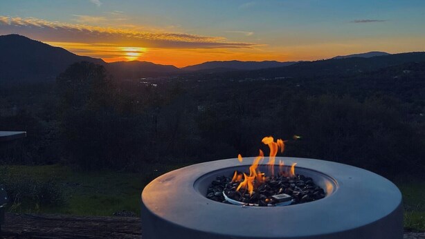 Un foyer avec des flammes, installé devant un paysage de vallée et de montagnes illuminé par le coucher du soleil.
