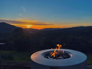A fire pit with flames, set against a sunset view of a valley and mountains. - New listing!! The Corner Views, Best view in town Yosemite Hot Tub & Pool table (Oakhurst)