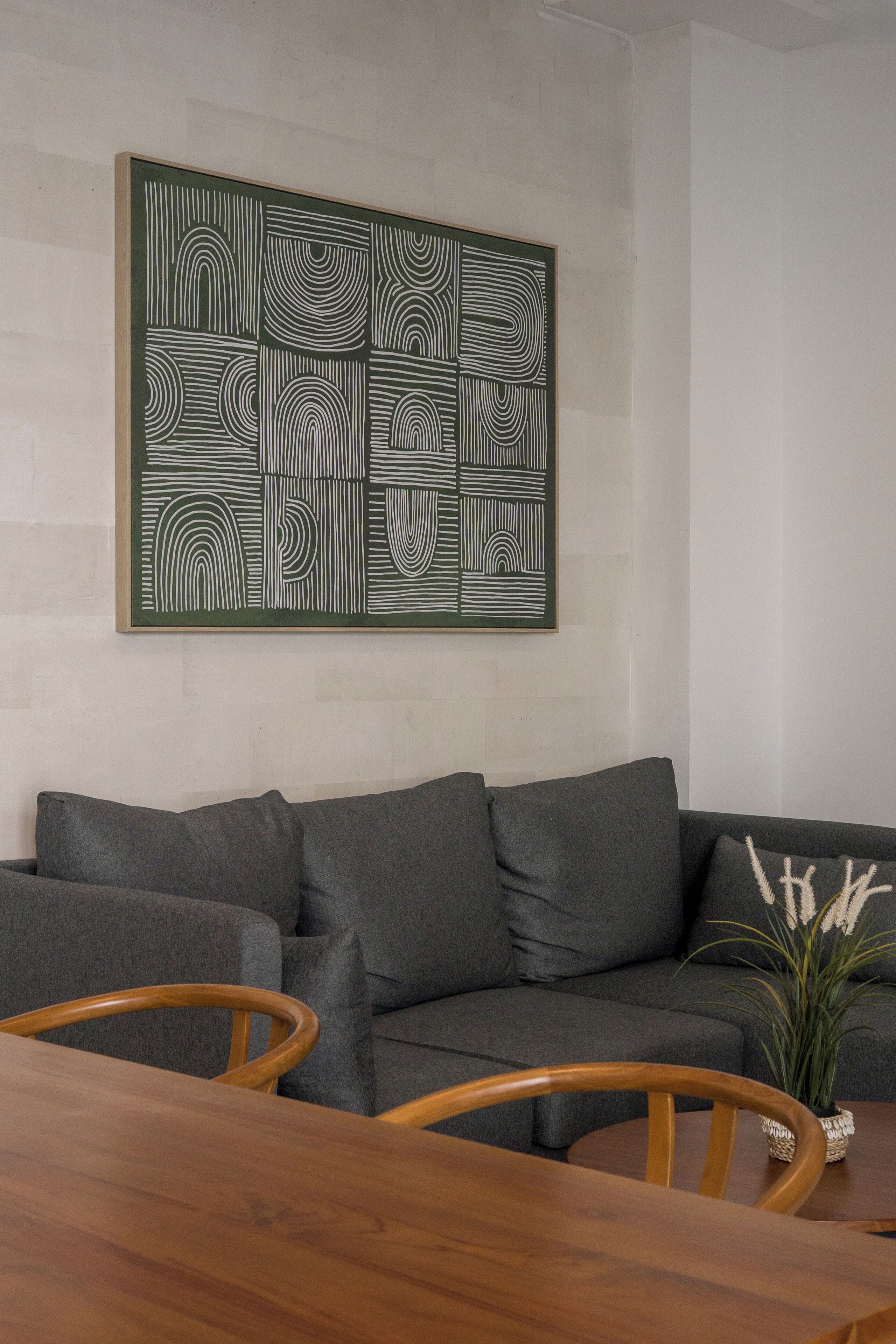 Uma sala de estar com sofá cinza, mesa de jantar de madeira e uma obra de arte abstrata emoldurada na parede.