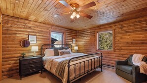 Ein Schlafzimmer in einer Blockhütte mit einem Bett, Nachttischen, einem Sessel und einem Deckenventilator.