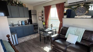 A modern living room with a dark brown leather sofa, a wooden staircase, and a kitchen area with grey cabinets and a black refrigerator. - Cozy cottage with fresh baked goods (Colorado City)