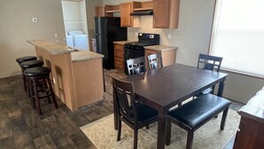 Una cocina compacta con armarios de madera, un refrigerador negro, una estufa y un comedor con mesa y sillas.