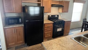 Una cocina compacta con armarios de madera, un refrigerador negro, un microondas y una estufa.