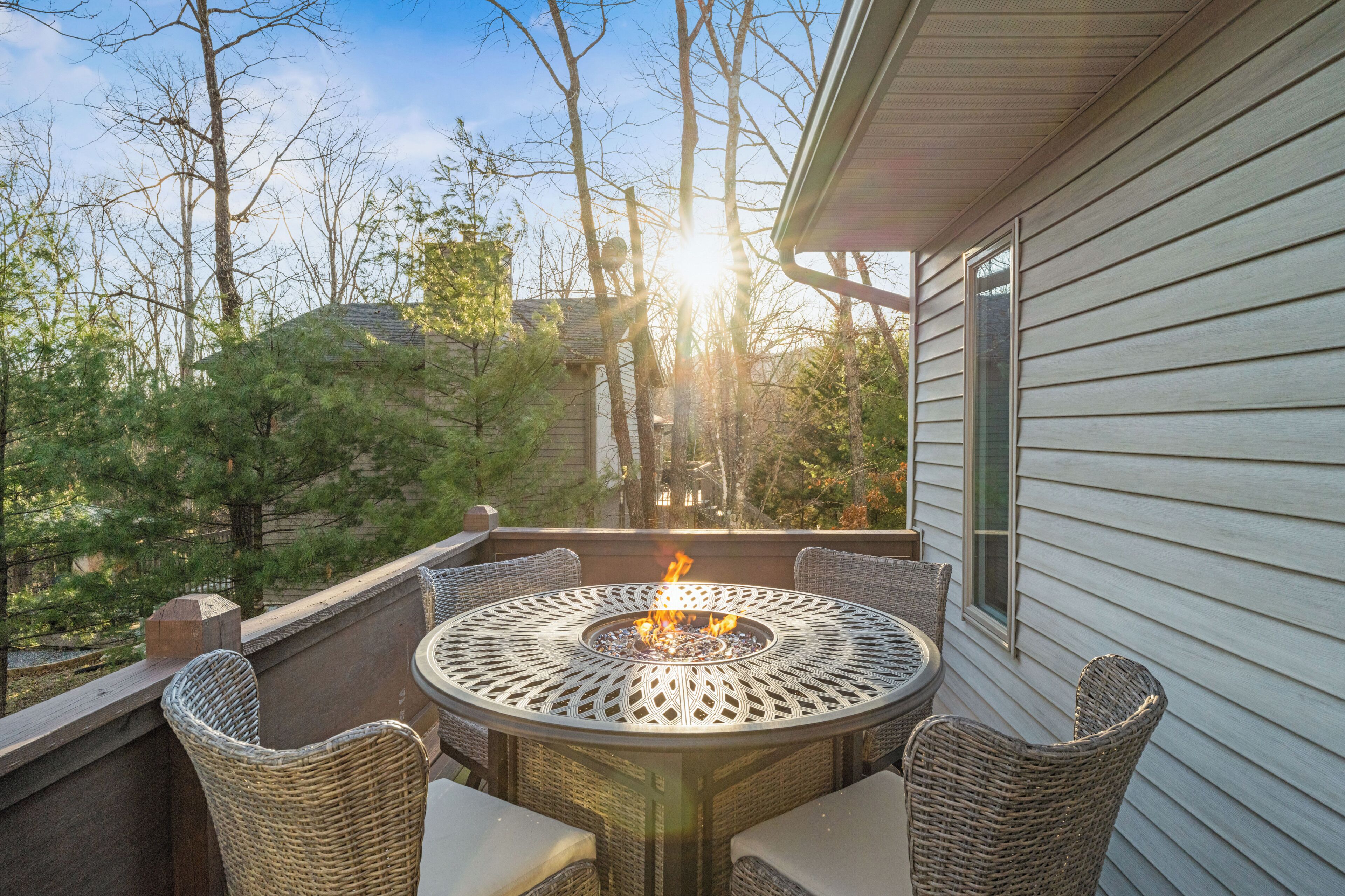 Een terras met een ronde tafel en stoelen, een vuurkorf en uitzicht op bomen en een huis.