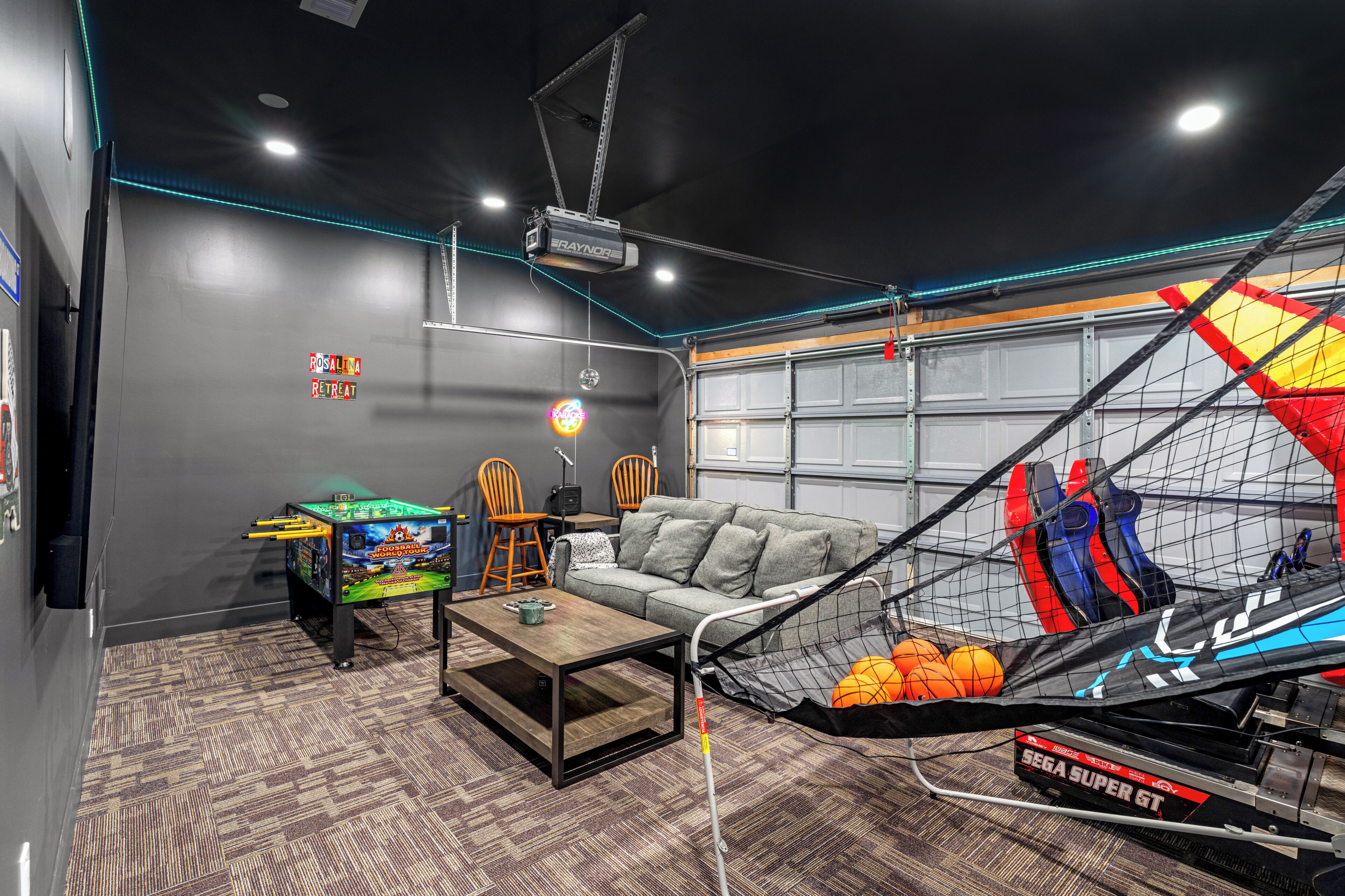 A room with a sofa, a coffee table, a projector, a gaming chair, and a hammock with sports balls.