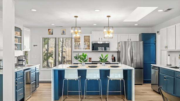 Cozinha moderna com ilha central, banquetas, eletrodomésticos de aço inoxidável e iluminação pendente.