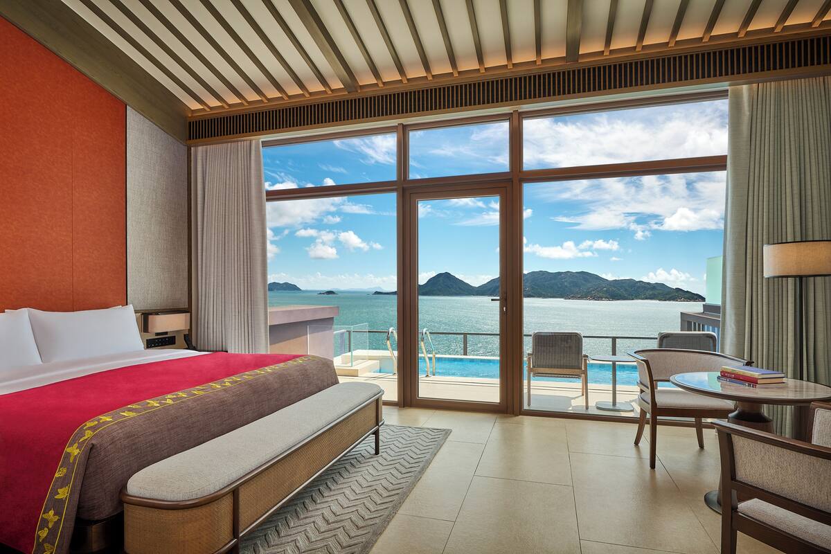 Ein Hotelzimmer mit einem großen Bett, einer Sitzecke mit Meerblick und einem Balkon mit Pool.