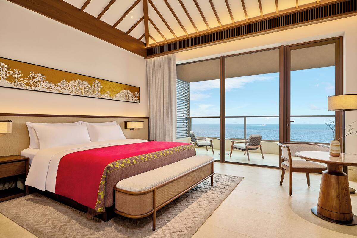 Ein Hotelzimmer mit Bett, einem Balkon mit Meerblick und einem Tisch mit Stühlen.