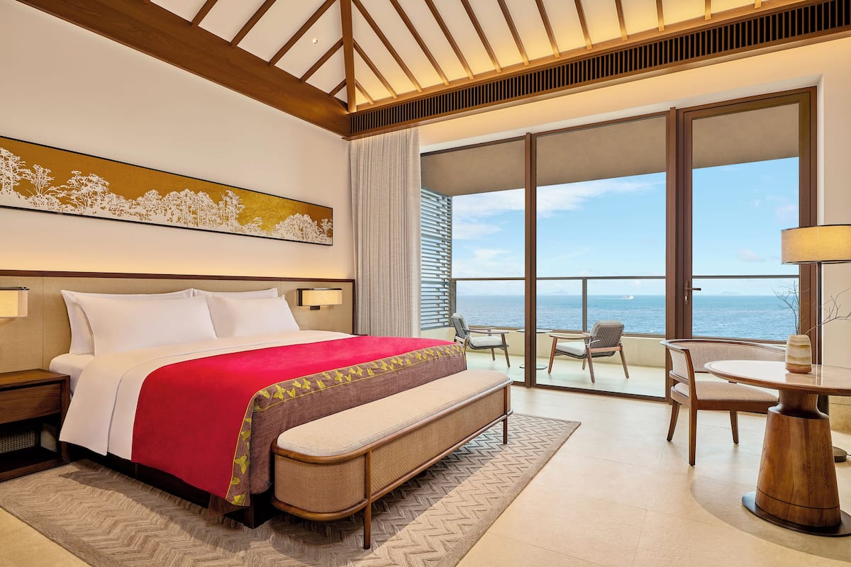 Une chambre d’hôtel avec un lit, un balcon donnant sur la mer et une table avec des chaises.