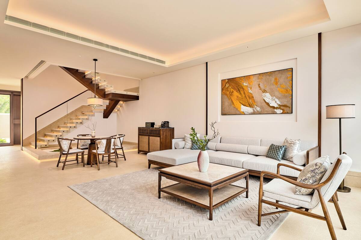 Ein modernes Wohnzimmer mit Sofa, Couchtisch und Sesseln, einer Treppe und einem großen abstrakten Gemälde an der Wand.