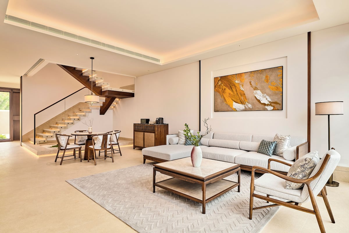 Un salon moderne avec un canapé, une table basse et des fauteuils, un escalier et un grand tableau abstrait accroché au mur.