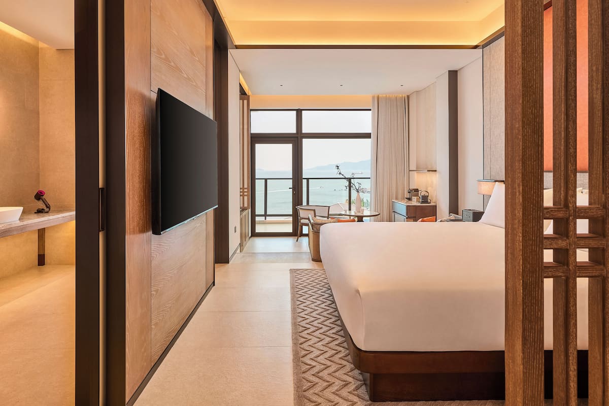 Une chambre d’hôtel moderne dotée d’un grand lit, d’une télévision, d’un bureau avec une chaise et offrant une vue sur la mer.