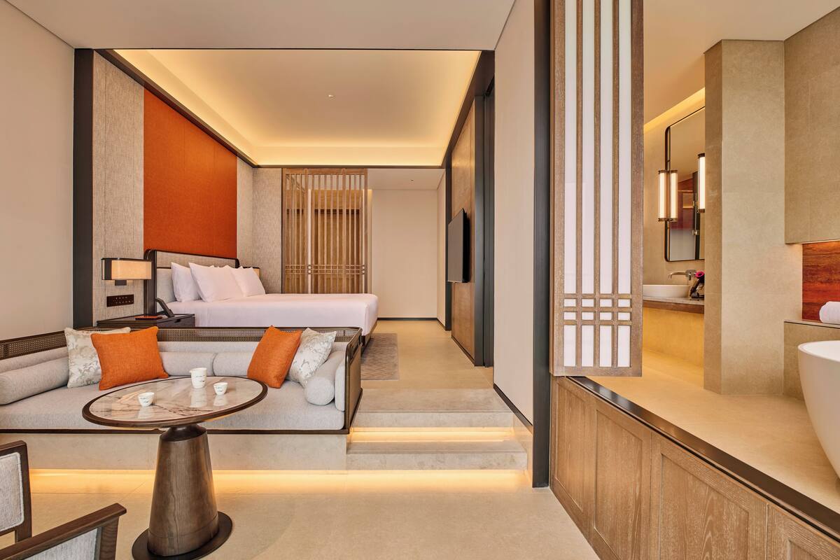 Ein Hotelzimmer mit Bett, Sofa, Couchtisch und einem Badezimmer mit Waschbecken und Spiegel.