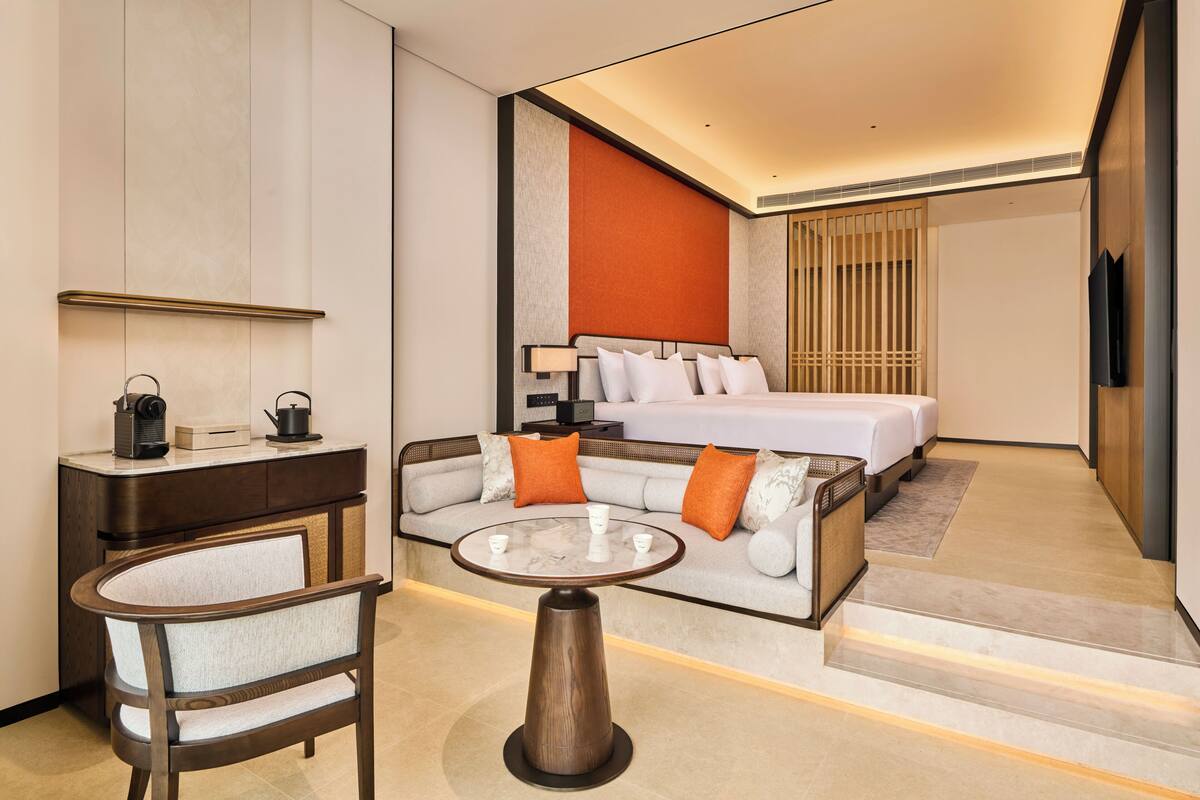 Ein modernes Hotelzimmer mit Schlafsofa, Esstisch, Schreibtisch mit Stuhl und Fernseher.