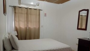 Un dormitorio con cama, mesita de noche, espejo y aire acondicionado de pared.