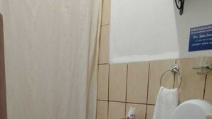 Ένα μικρό μπάνιο με τουαλέτα, κάδο απορριμμάτων, διανομέα πετσετών και κουρτίνα για το ντους.