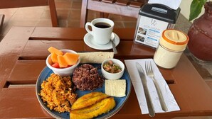 Un plato de desayuno con diversos alimentos, una taza de café, un tarro de azúcar y un menú sobre una mesa de madera.