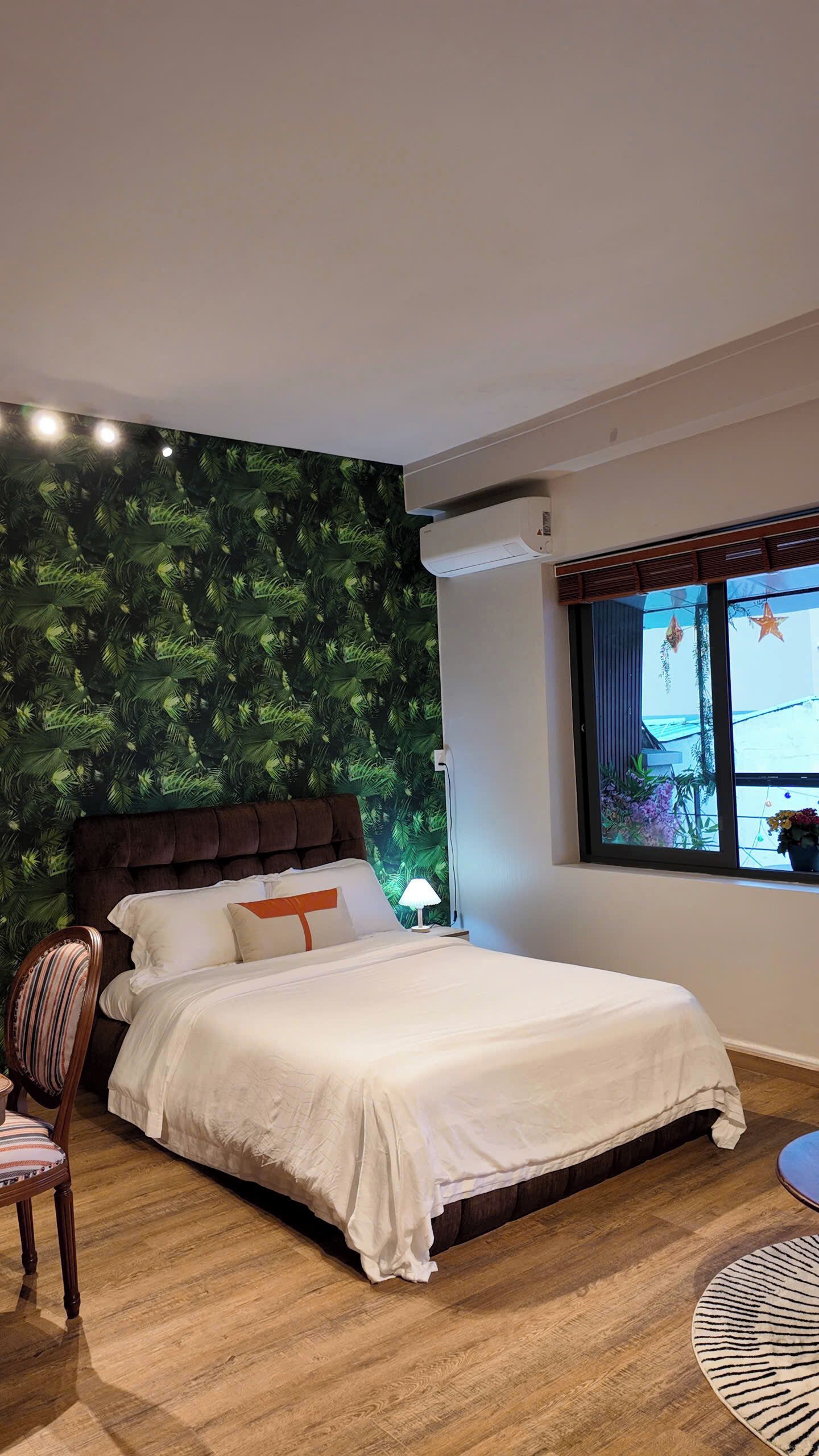 A bedroom with a bed, a chair, a window with a view, and a wall with a leaf pattern.