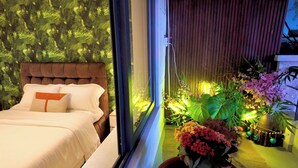 A bedroom with a large bed, a window, and a view of a garden with various plants and flowers. - 1 BR Nguyen Hue Walking St Bitexco (Ho Chi Minh City)