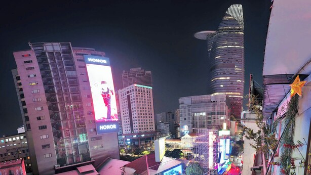 A nighttime cityscape with illuminated billboards, including one for HONOR, and a variety of buildings with different architectural styles. - 1 BR Nguyen Hue Walking St Bitexco (Ho Chi Minh City)