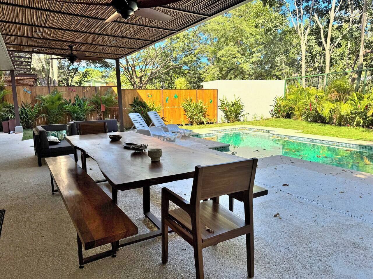 Une terrasse extérieure avec une piscine, des meubles en bois et un espace abrité doté d’un ventilateur de plafond.