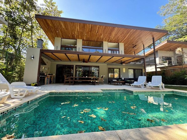 Una casa moderna amb piscina, mobiliari exterior i una zona de pati coberta.