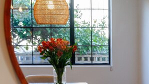 A dining area with a round table, chairs, a hanging rattan light fixture, and a window with a view of greenery. - Private 2BR Duplex  Parking, W/D, Near Studios (Los Angeles)